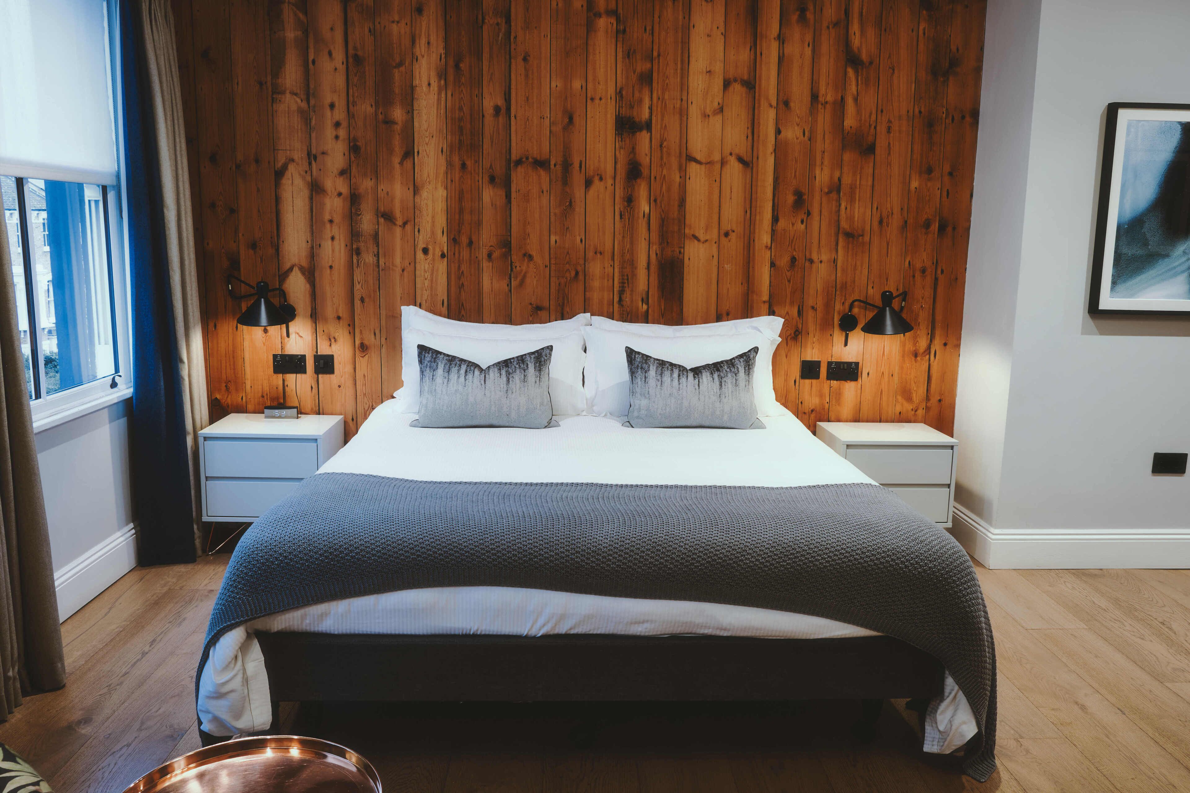 Una camera da letto con una testiera in legno a pannelli, un letto grande con due cuscini, un comodino con una lampada e una finestra con tende.