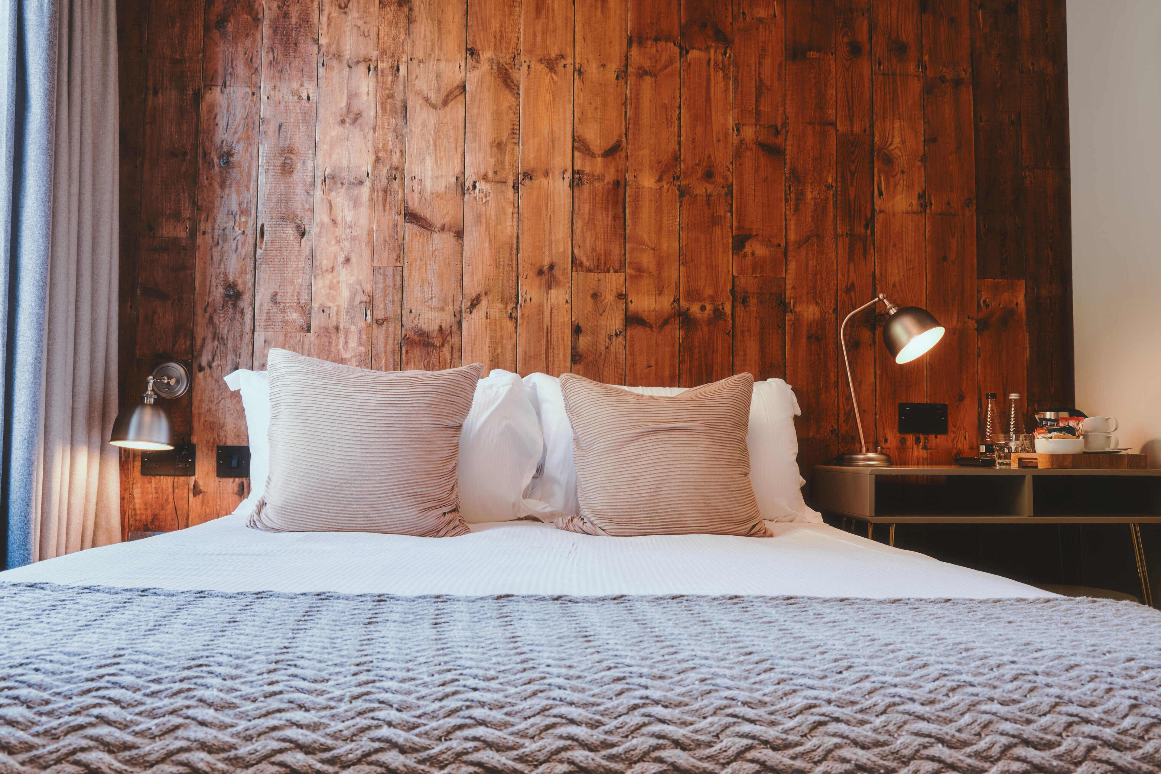 A neatly made bed with a textured blanket, a wooden headboard, and a bedside lamp.