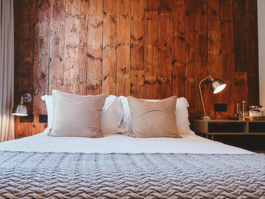 Uma cama bem arrumada com um cobertor texturizado, cabeceira de madeira e abajur.