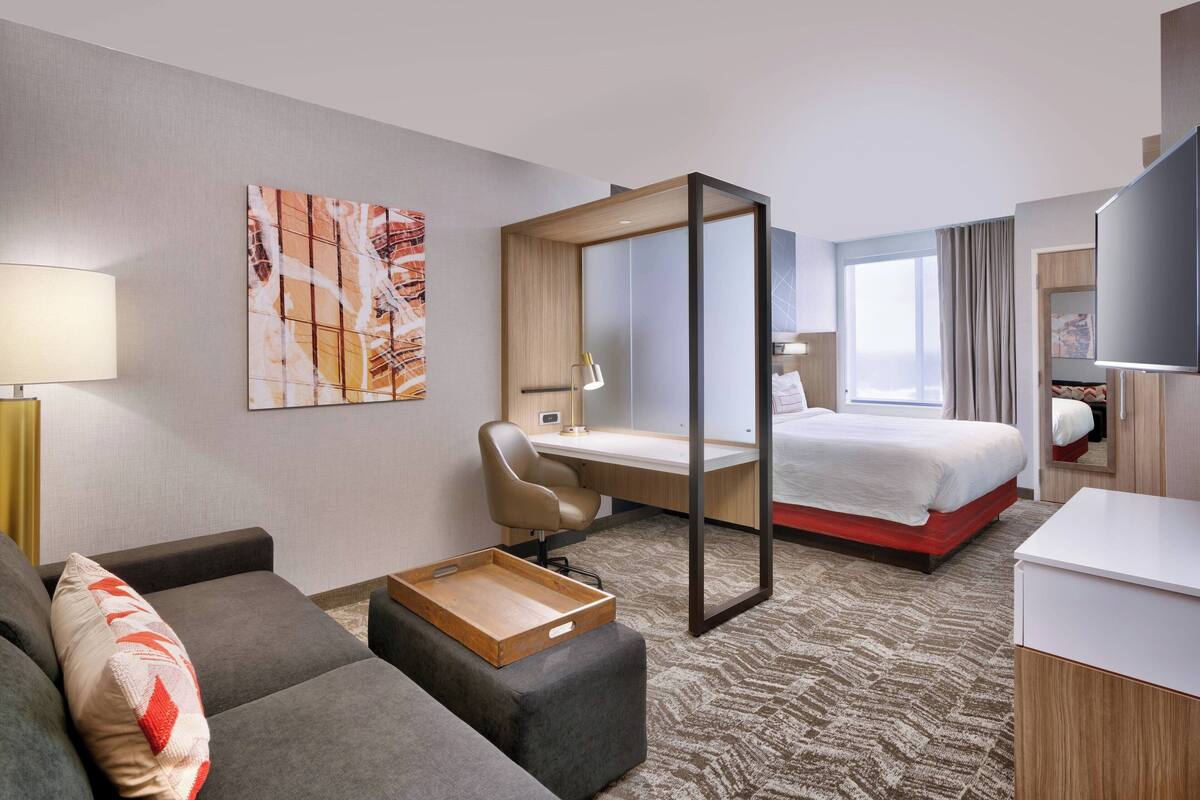 A hotel room with a bed, a desk, a chair, a sofa, a tray table, and a TV.
