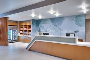 A modern reception area with a wooden reception desk, a large wall mural, and a refrigerated display case.