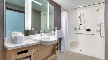 Un baño moderno con un espejo grande, dos lavamanos, una ducha con cabezal de ducha manual y un perchero para toallas.