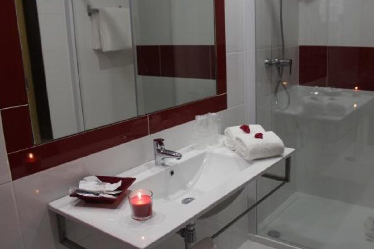 Une salle de bain moderne avec une douche à l’italienne en verre, un lavabo blanc avec un miroir et une bougie rouge posée sur le comptoir.