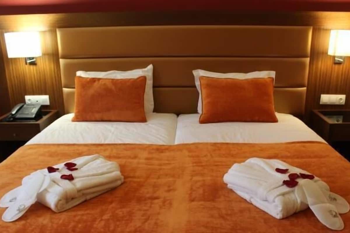 Una cama doble con dos almohadas, un cabecero de madera y dos mesitas de noche con lámparas.
