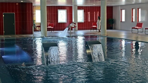 Une piscine intérieure dotée de jets d’eau, de murs rouges et de quelques chaises.