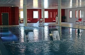 Une piscine intérieure dotée de jets d’eau, de murs rouges et de quelques chaises.
