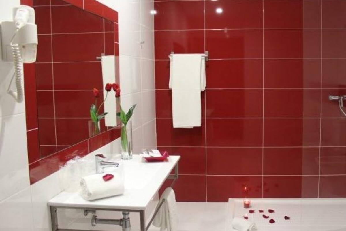 Une salle de bain moderne avec une douche carrelée de carreaux rouges, un lavabo blanc avec un miroir et une paroi de douche en verre.