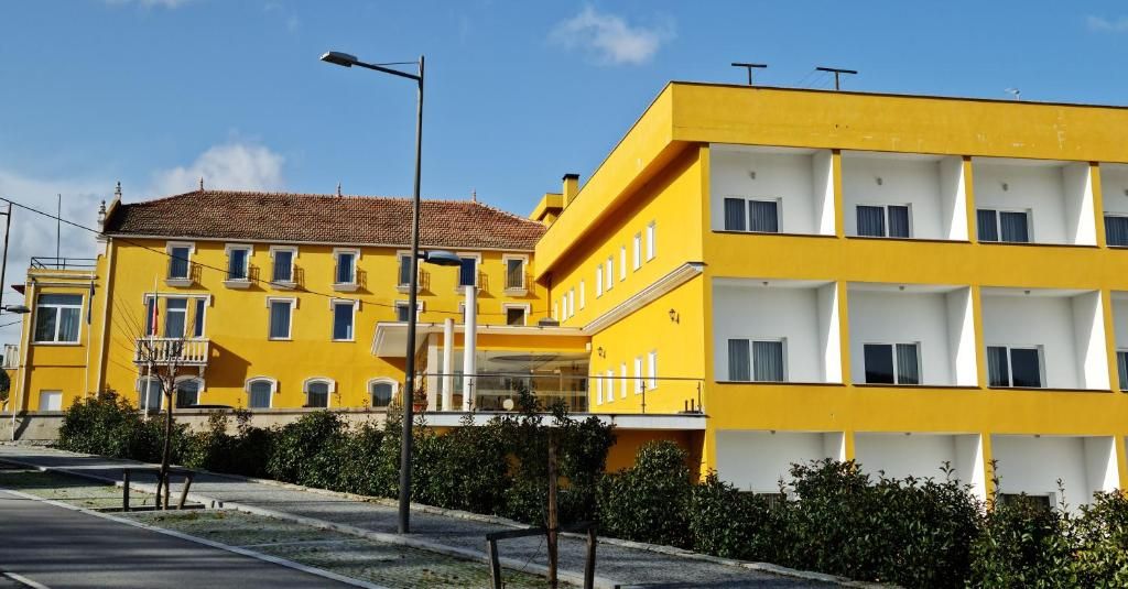 Un edificio amarillo de varios pisos y balcones, cielo despejado y una calle en primer plano.