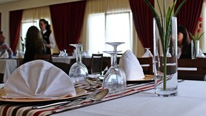 Une table à manger dressée avec une nappe blanche, des assiettes, des couverts et un vase rempli de fleurs rouges.