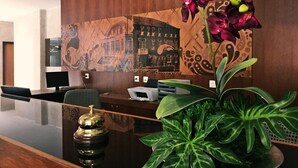 Un comptoir d’accueil avec un revêtement en bois, une grande plante en pot et un téléphone d’époque.