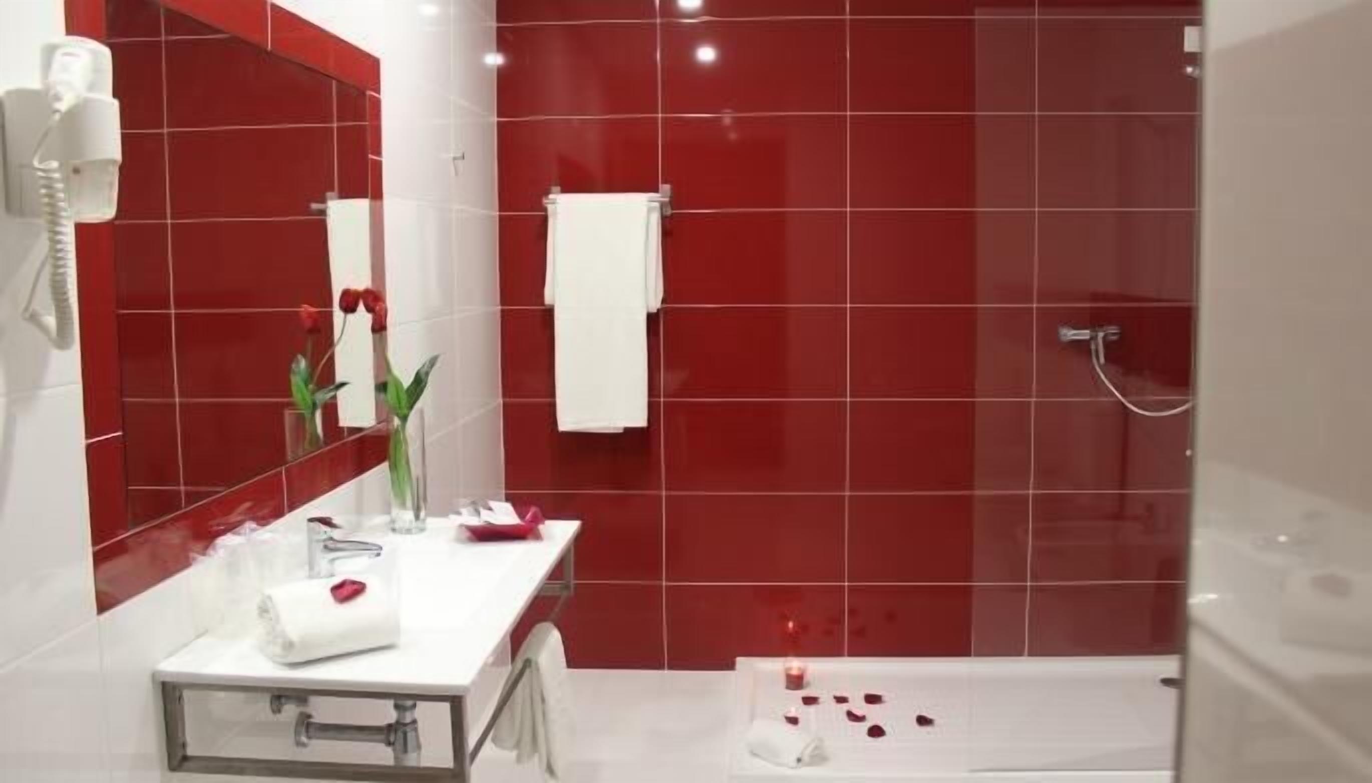 Un baño moderno con azulejos rojos, un lavamanos blanco, un espejo y una zona de ducha.