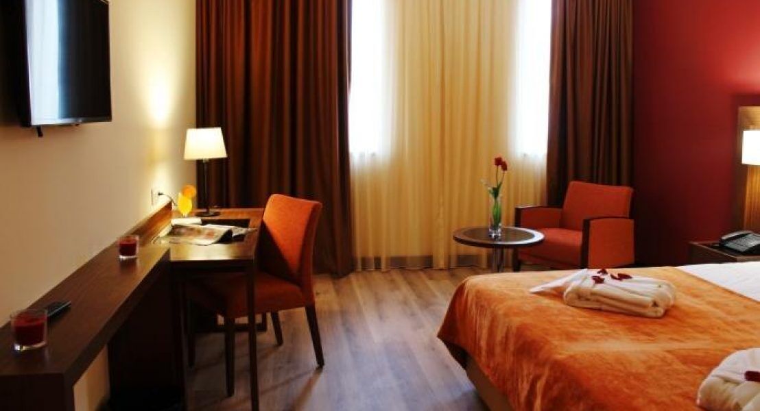 Habitación de hotel con una cama, un escritorio, una silla, una mesita y un televisor.