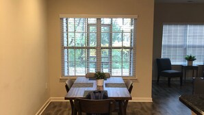 A dining area with a table and chairs, a window with blinds, and a plant on the table. - Cozy, Quiet and Well Appointed Dual Master w/  2.5 ba Townhome 4 miles to GSO!! (Greensboro)