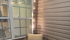 A corner seating area with a cushioned chair and a small table, a window with blinds, and string lights. - Cozy, Quiet and Well Appointed Dual Master w/  2.5 ba Townhome 4 miles to GSO!! (Greensboro)