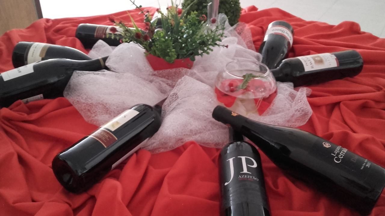 Une table sur laquelle sont disposées plusieurs bouteilles de vin et un verre, le tout posé sur une nappe rouge, avec une petite plante en pot à proximité.