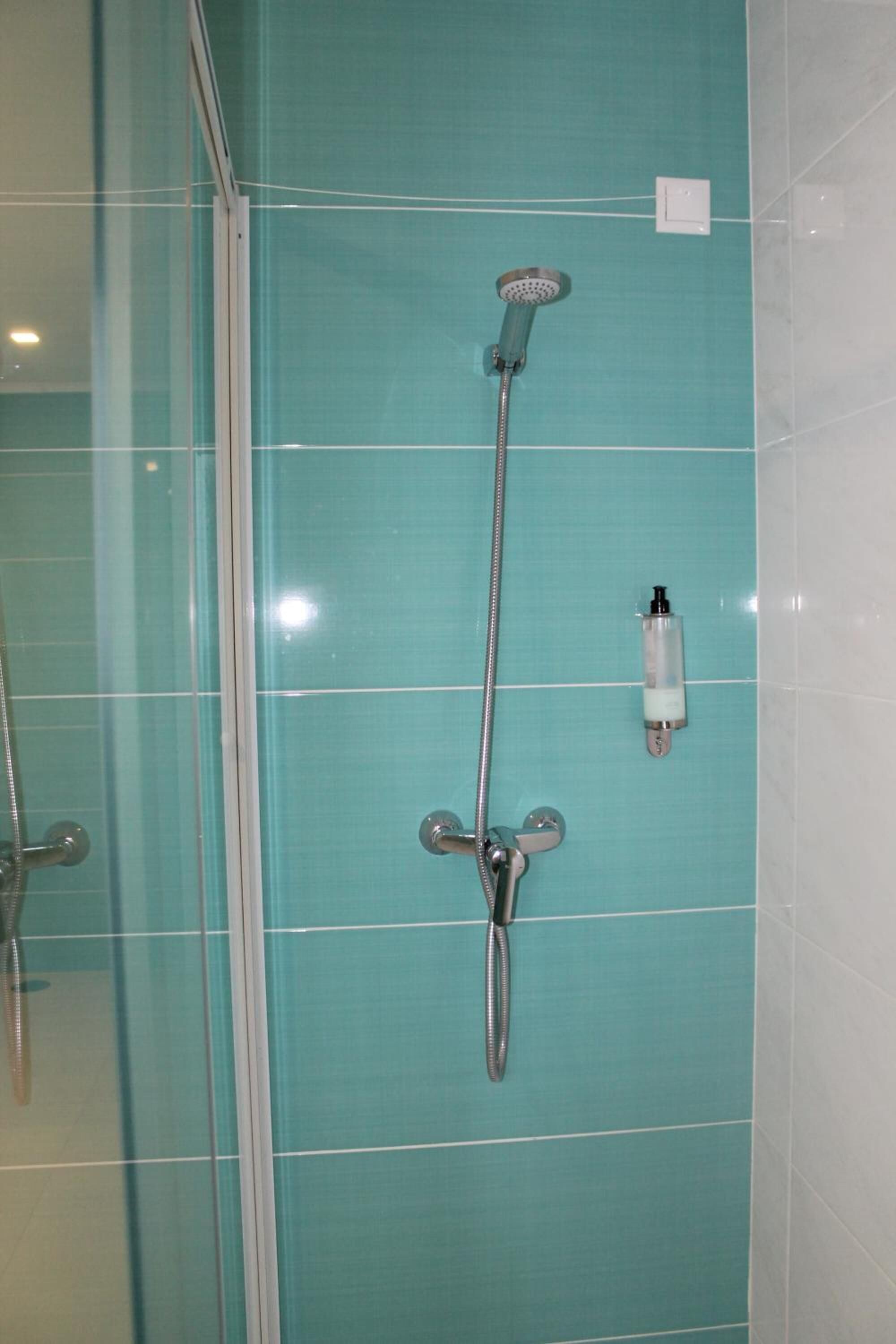 Een badkamer met een douche, een glazen deur en een zeepdispenser aan de muur.