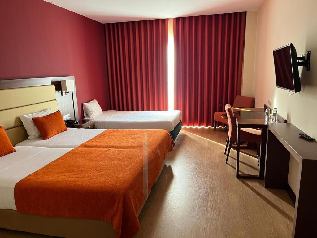 A hotel room with two beds, a desk, a chair, a TV, and a window with curtains.