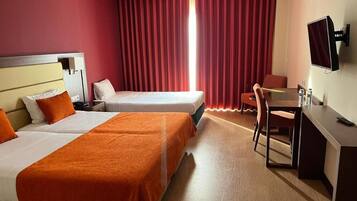 A hotel room with two beds, a desk, a chair, a TV, and a window with curtains.