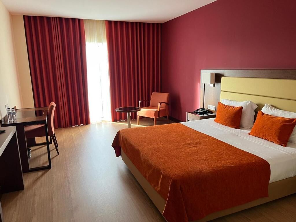 A hotel room with a bed, a desk, a chair, and a small table.