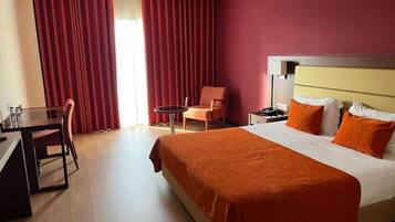 A hotel room with a bed, a desk, a chair, and a small table.