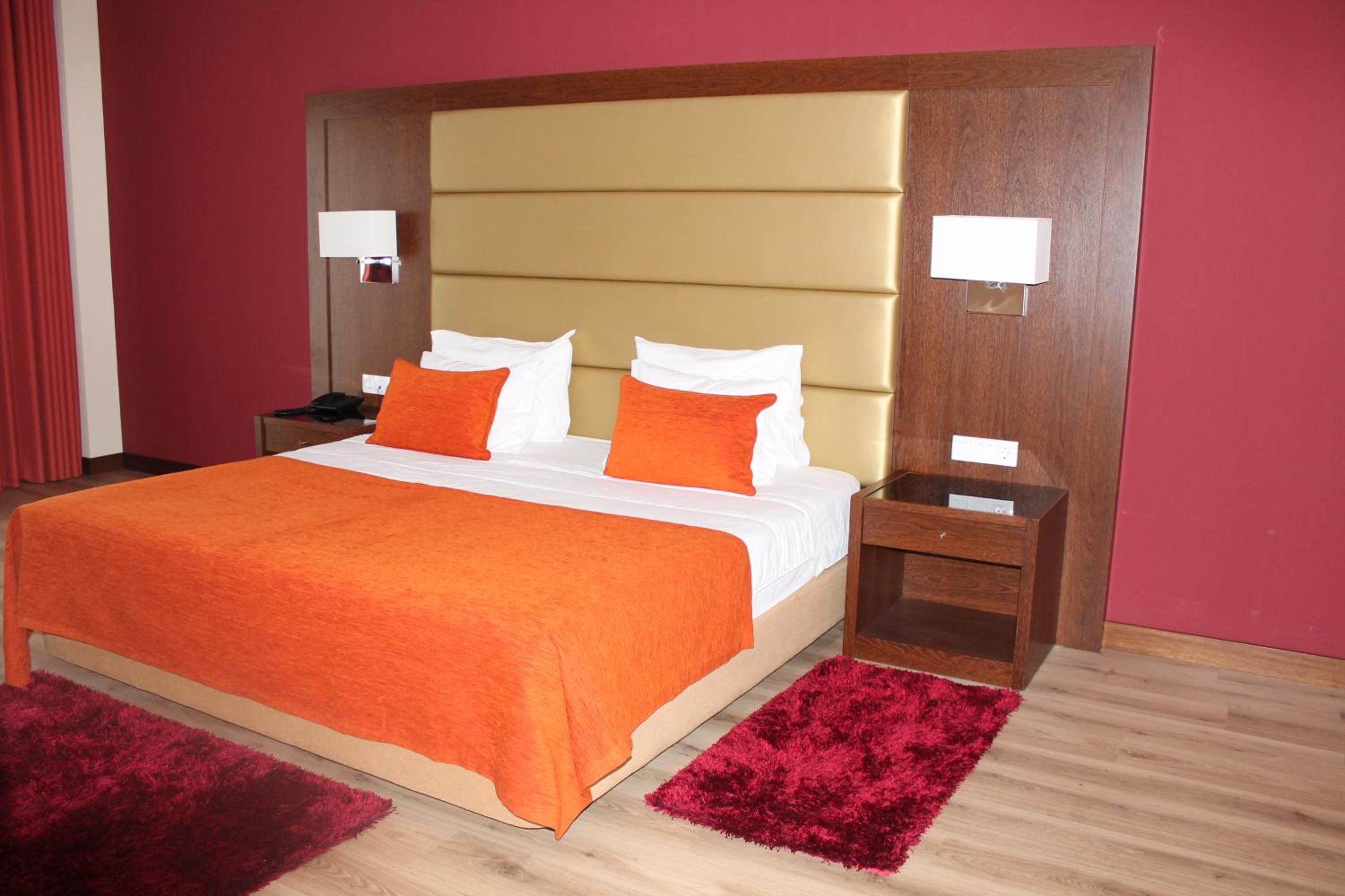 A hotel room with a large bed, two nightstands, a wooden headboard, and a red carpet.