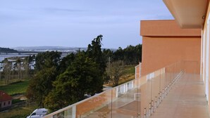 Un bâtiment moderne doté d’un balcon en verre donnant sur un plan d’eau et des arbres.