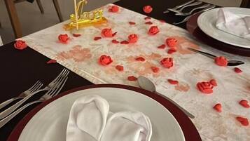 A dining table set with a heart-shaped napkin, red rose petals, and a heart-shaped napkin holder with the word 'Amor'.
