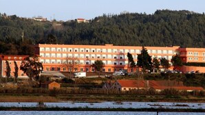Un hôtel à plusieurs étages, doté d’une façade uniforme, situé près d’une étendue d’eau et entouré d’arbres.
