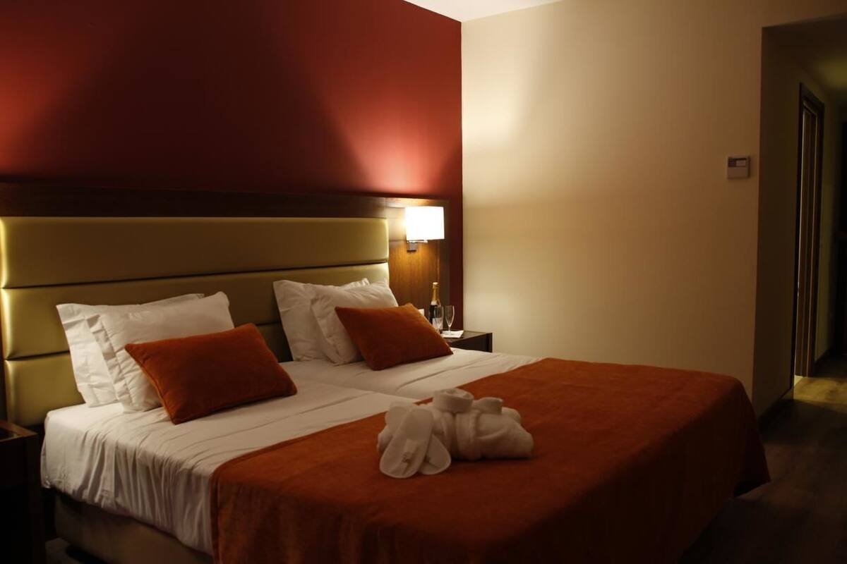 Ein Hotelzimmer mit einem großen Bett, einem Nachttisch mit einer Lampe und einer Tür rechts.