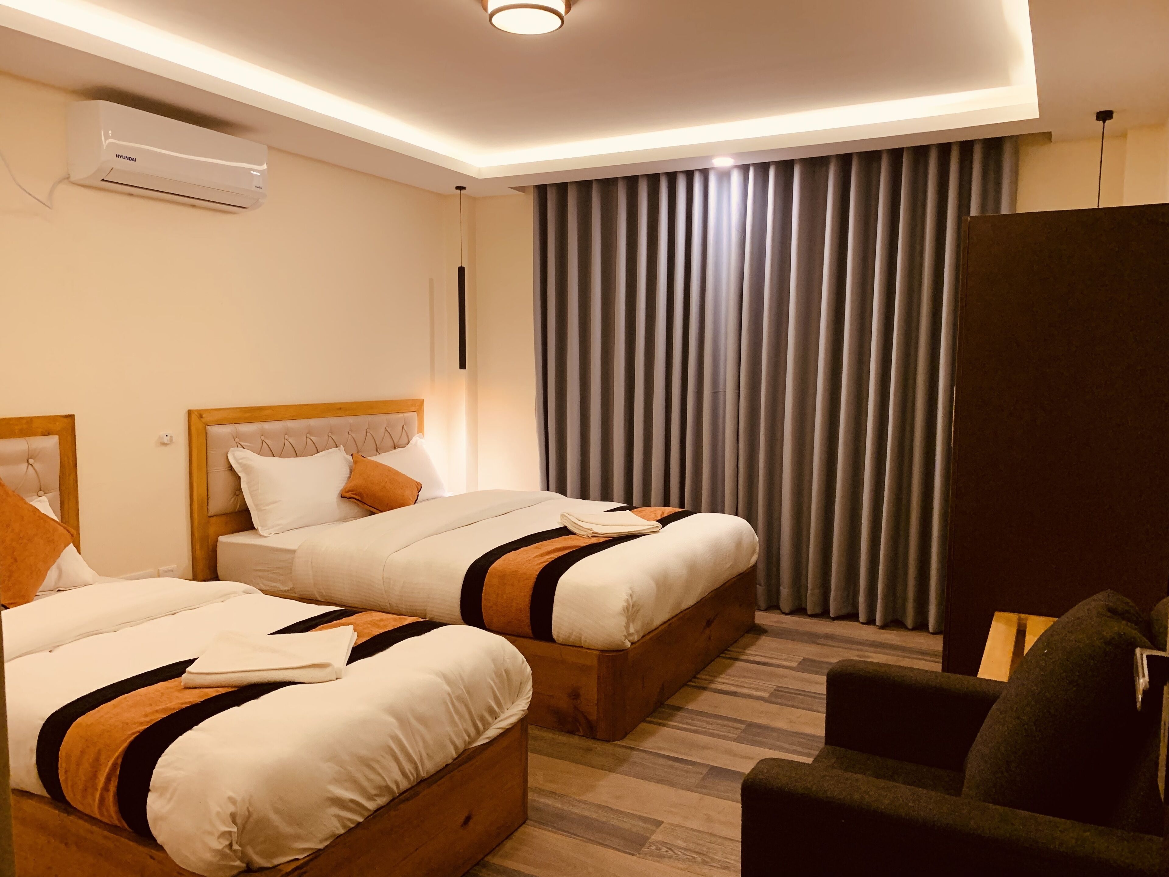 Una habitación de hotel con dos camas, un cabecero de madera, un ventanal con cortinas y un aire acondicionado instalado en la pared.