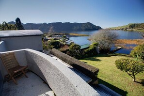 A balcony with a chair, a view of a lake, and a building with a sloped roof.