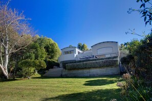 A modern two-story house with a sloped roof, a well-maintained lawn, and a variety of trees and shrubs.