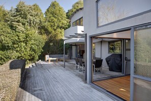 A modern house with a wooden deck, outdoor seating, and a covered patio area.