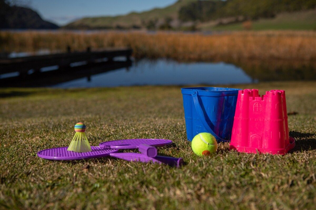 A grassy area with a blue and pink bucket, a purple shuttlecock, and a tennis ball.