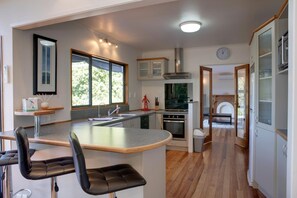 Una cocina moderna con una isla central, taburetes de bar, horno empotrado y vistas al exterior.