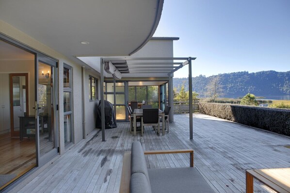 A covered outdoor area with a table and chairs, a sofa, and a view of a lake and hills.