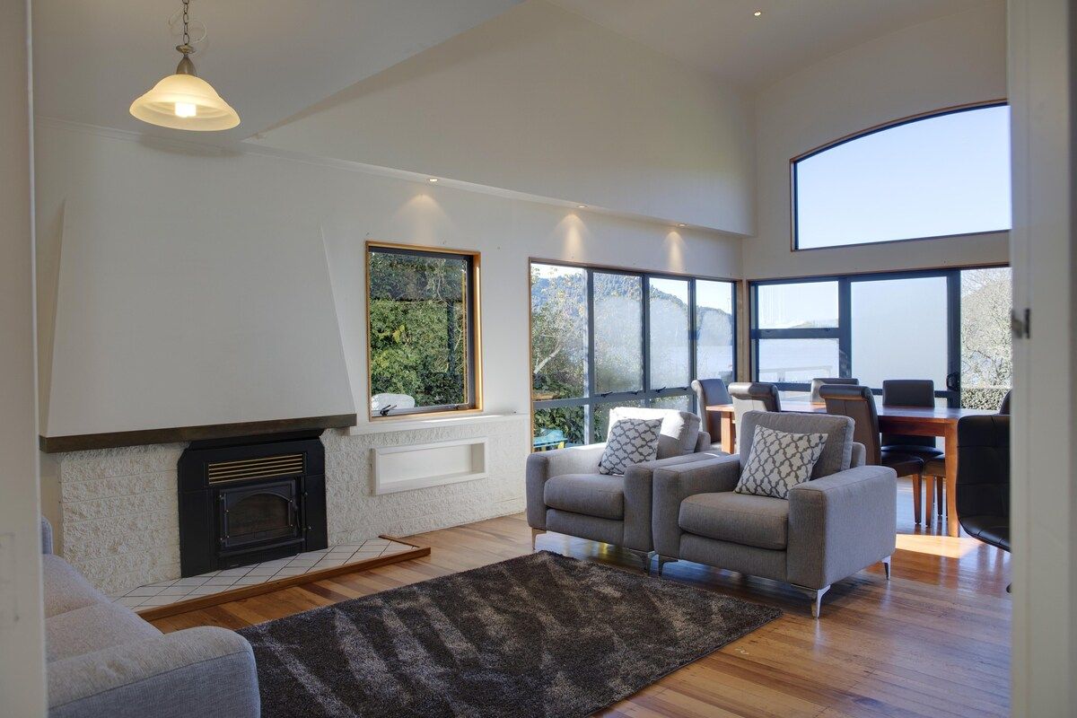 A modern living room with a fireplace, a sofa set, and large windows offering a view of the outdoors.