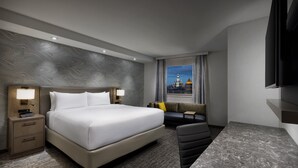 A hotel room with a large bed, a desk, a chair, a nightstand, and a view of a cityscape through the window. - Residence Inn by Marriott New York Downtown Manhattan/Financial District (New York)
