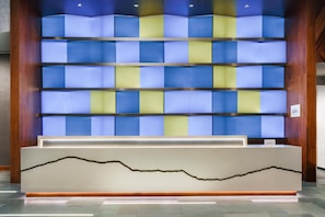 Welcome to our reception area, featuring a sleek reception desk and a vibrant backdrop of blue and yellow panels.