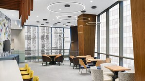 A modern cafe with round tables and chairs, large windows, and a wooden accent wall. - Residence Inn by Marriott New York Downtown Manhattan/Financial District (New York)