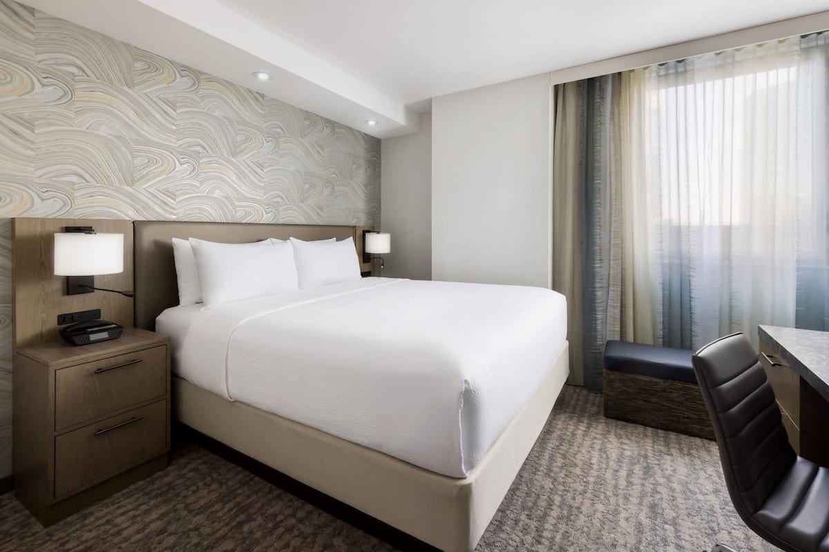 A hotel room with a large bed, bedside tables, a desk, and a chair.