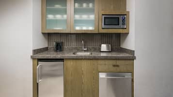 A compact kitchen with wooden cabinets, a microwave, a sink, a coffee maker, and a dishwasher.