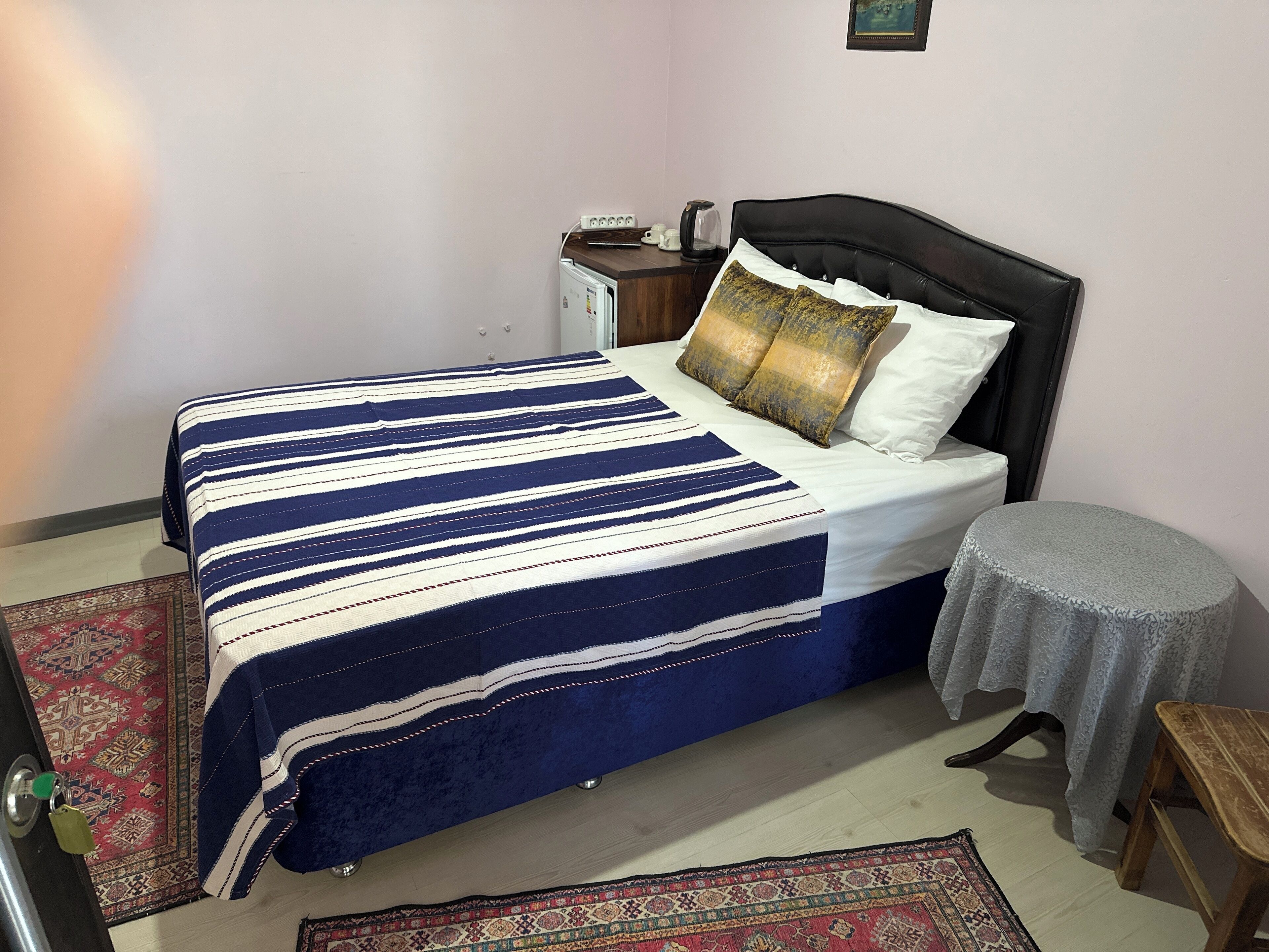 A bed with a striped bedspread, a nightstand with a lamp, and a small round table with a lace tablecloth.
