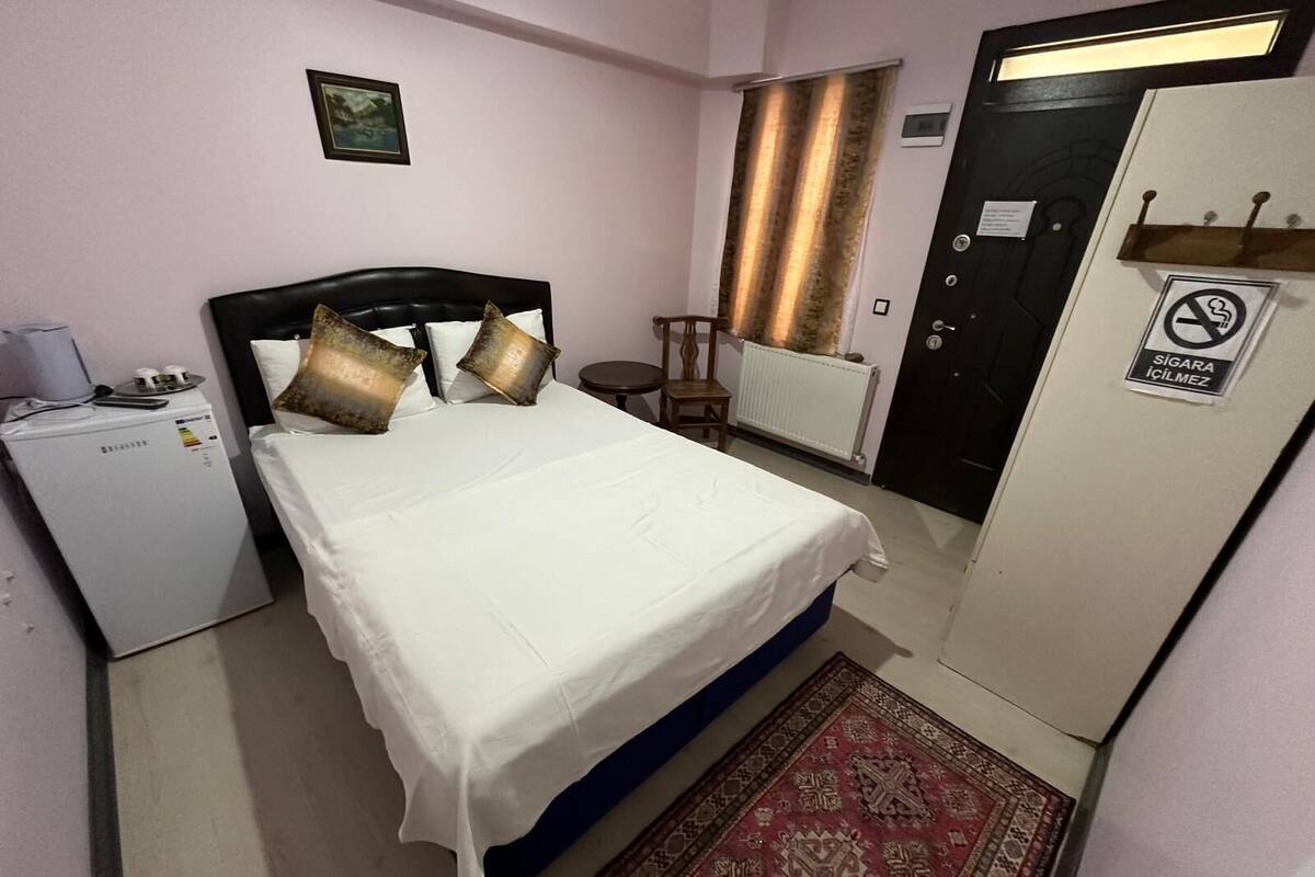 Un dormitorio pequeño y ordenado, con cama, escritorio pequeño, radiador y puerta con letrero de prohibido fumar.