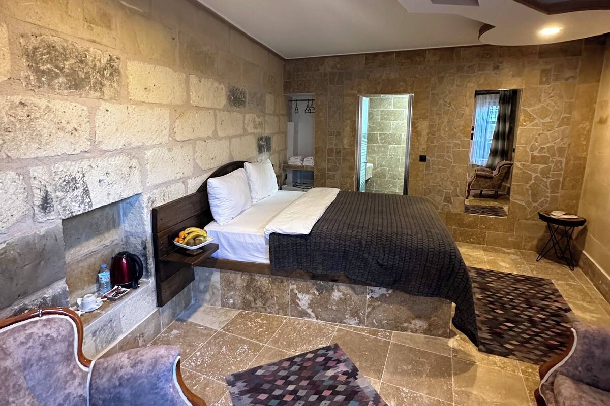 Un dormitorio con pared de piedra, una cama, una silla, una mesita y un tapete estampado.