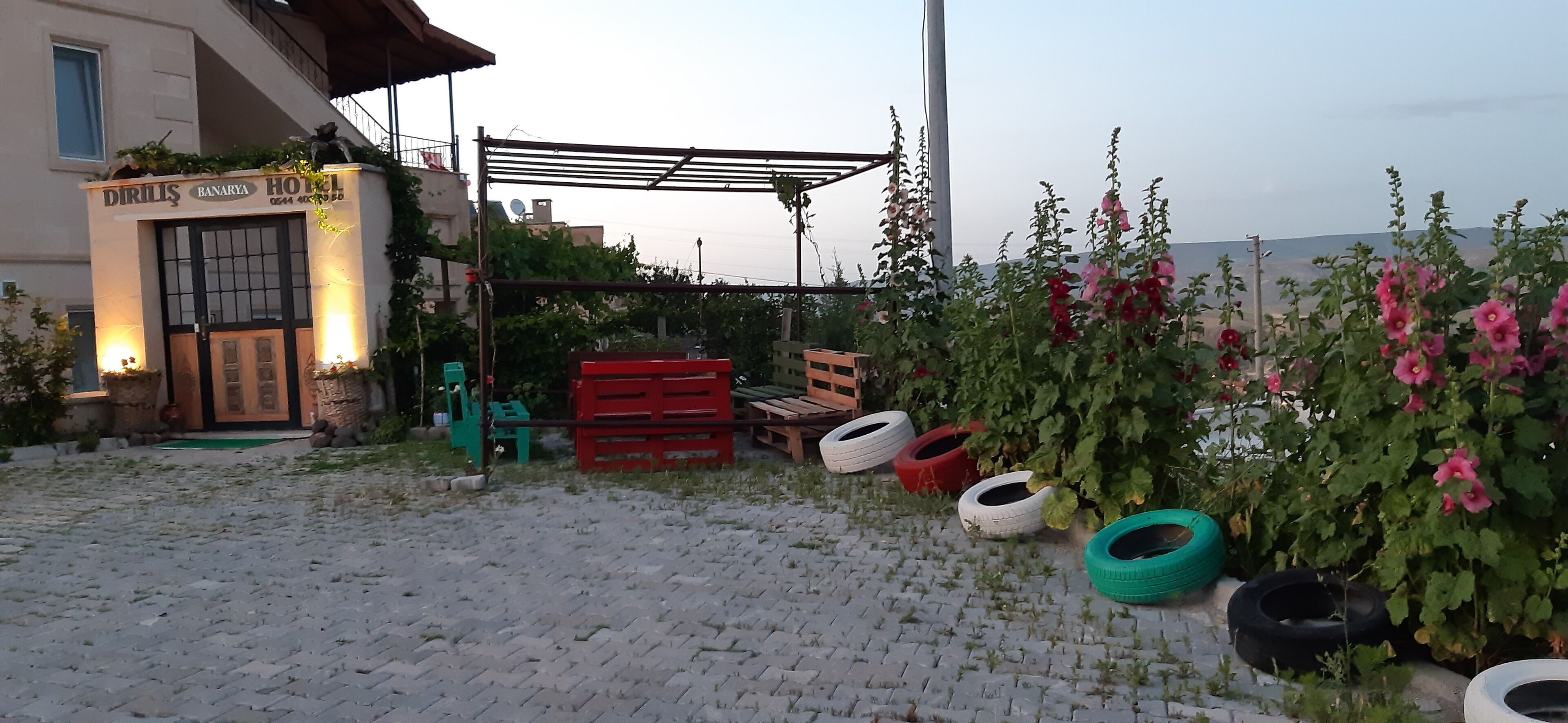A hotel entrance with a sign, a covered outdoor seating area, and tire planters with flowers.