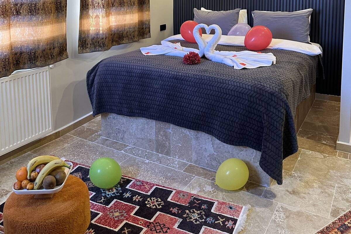 Un dormitorio moderno con cama, cortinas, una lámpara de techo, una lámpara de pared, un radiador, un frutero y globos en el suelo.