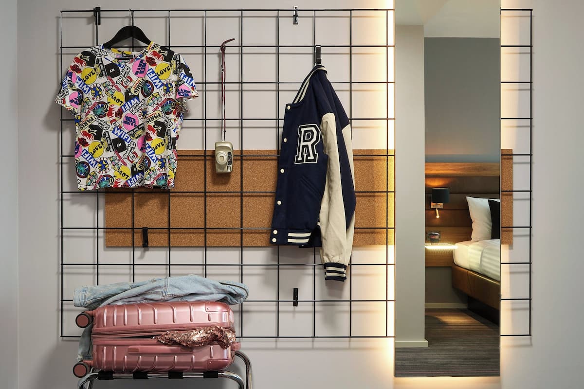 A hotel room with a bed, a bedside table, and a wall-mounted luggage rack.