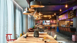 Un comedor amplio con una larga mesa de madera, varias sillas, lámparas colgantes y una zona de bar al fondo.