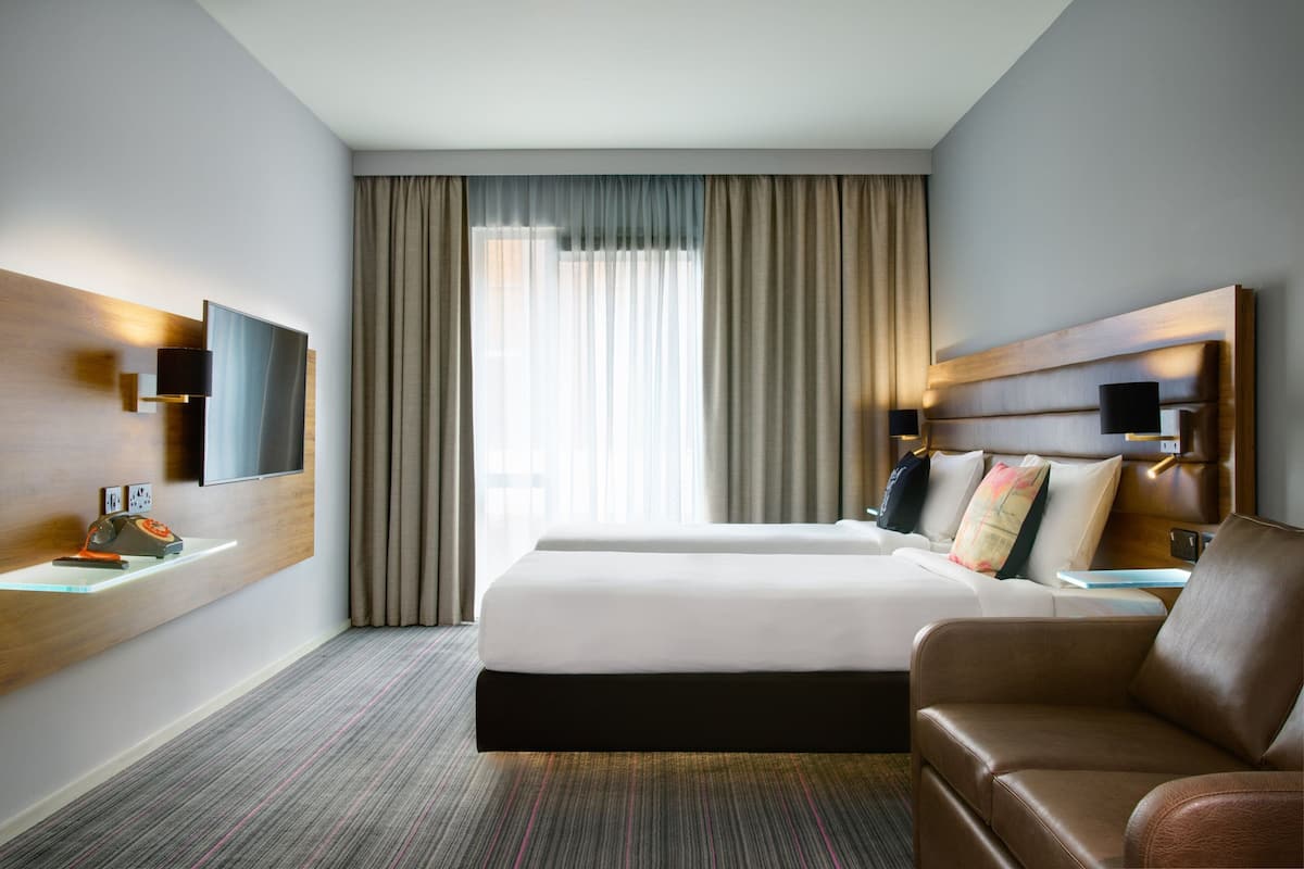 A hotel room with a large bed, a sofa, a TV mounted on the wall, and a desk with a telephone.